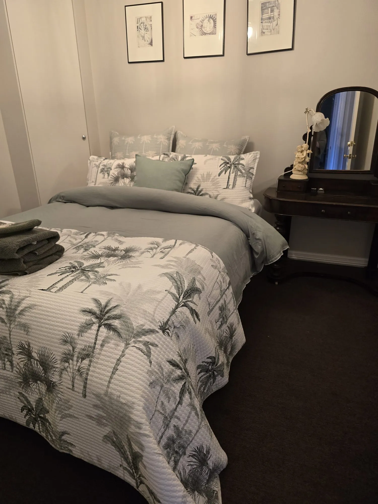 Second queen bedroom with a palm-print quilt beside an antique dressing table and mirror