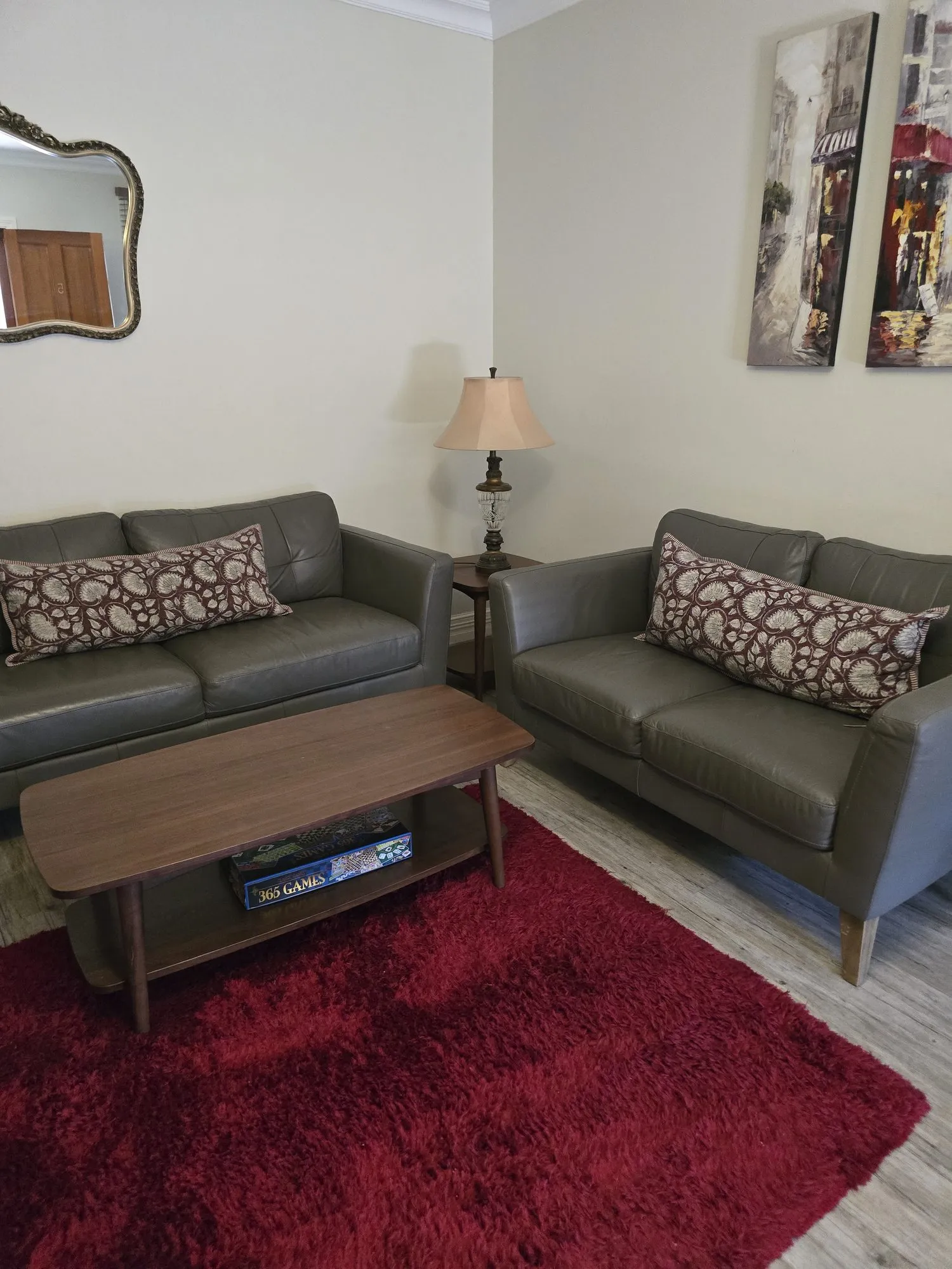 Two grey leather sofas with paisley cushions on a red rug beneath Paris street paintings