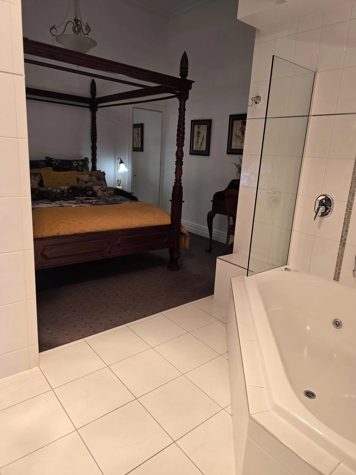 Corner spa bath and glass shower, with the four-poster bedroom beyond