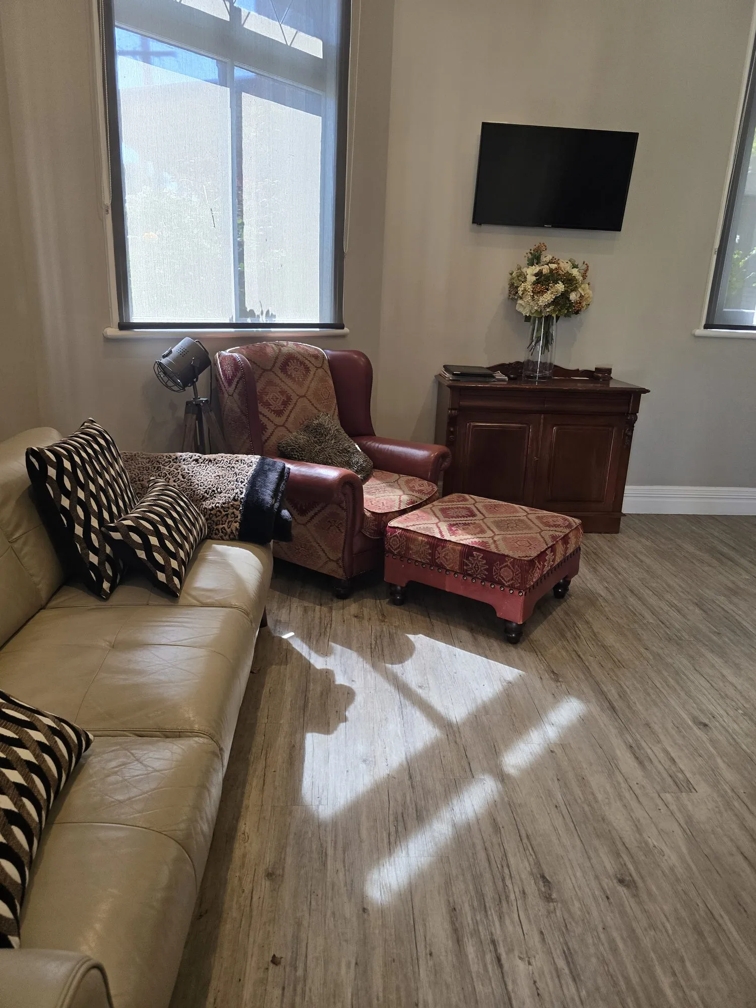 Sunlit living room with a leather sofa, a red armchair and footstool, and a timber sideboard