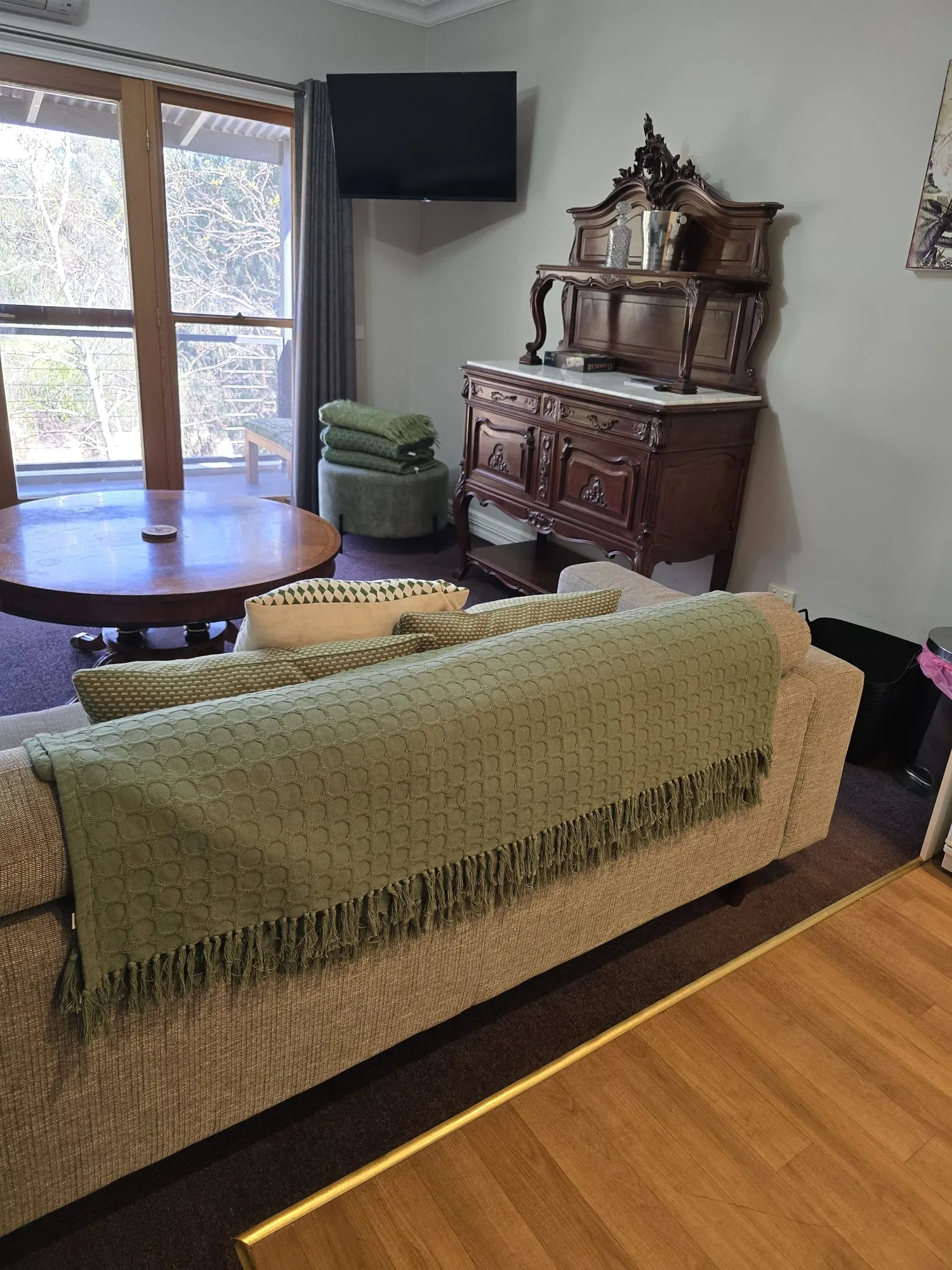 Living room with a sofa and green throw, a round table by the balcony window and an ornate dresser