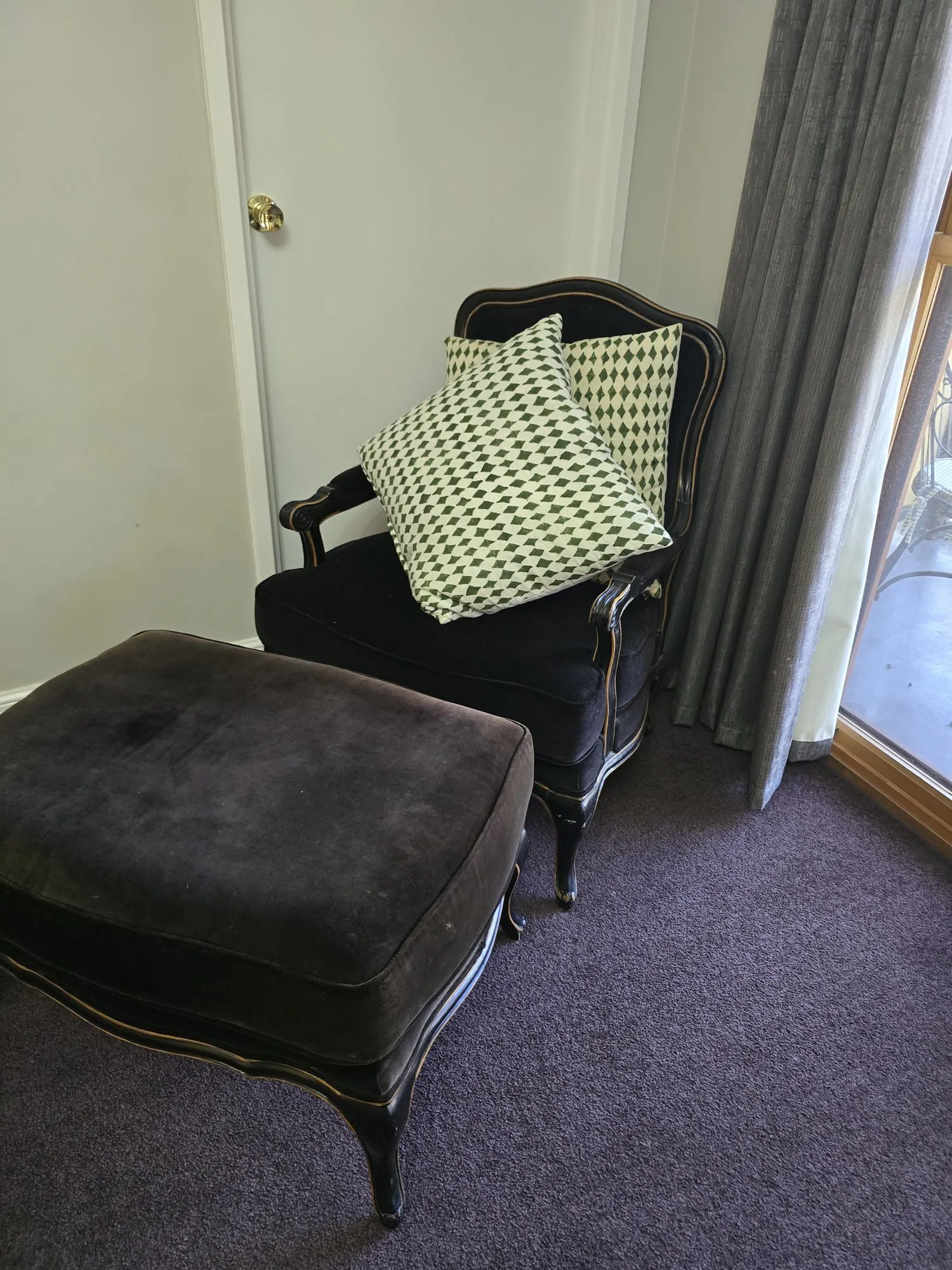Black velvet armchair and footstool with a green cushion beside the balcony door