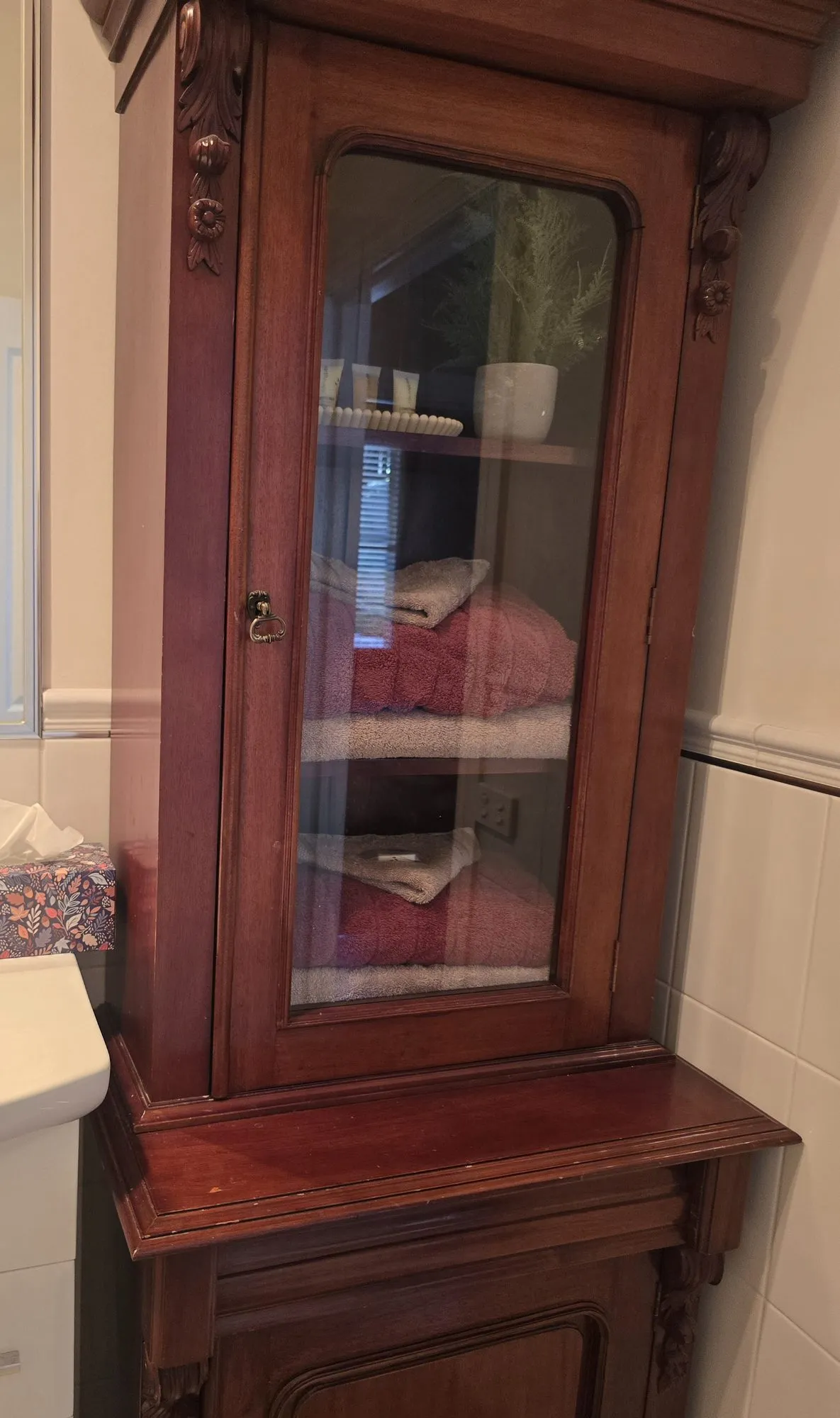 Glass-fronted antique cabinet stacked with fresh towels