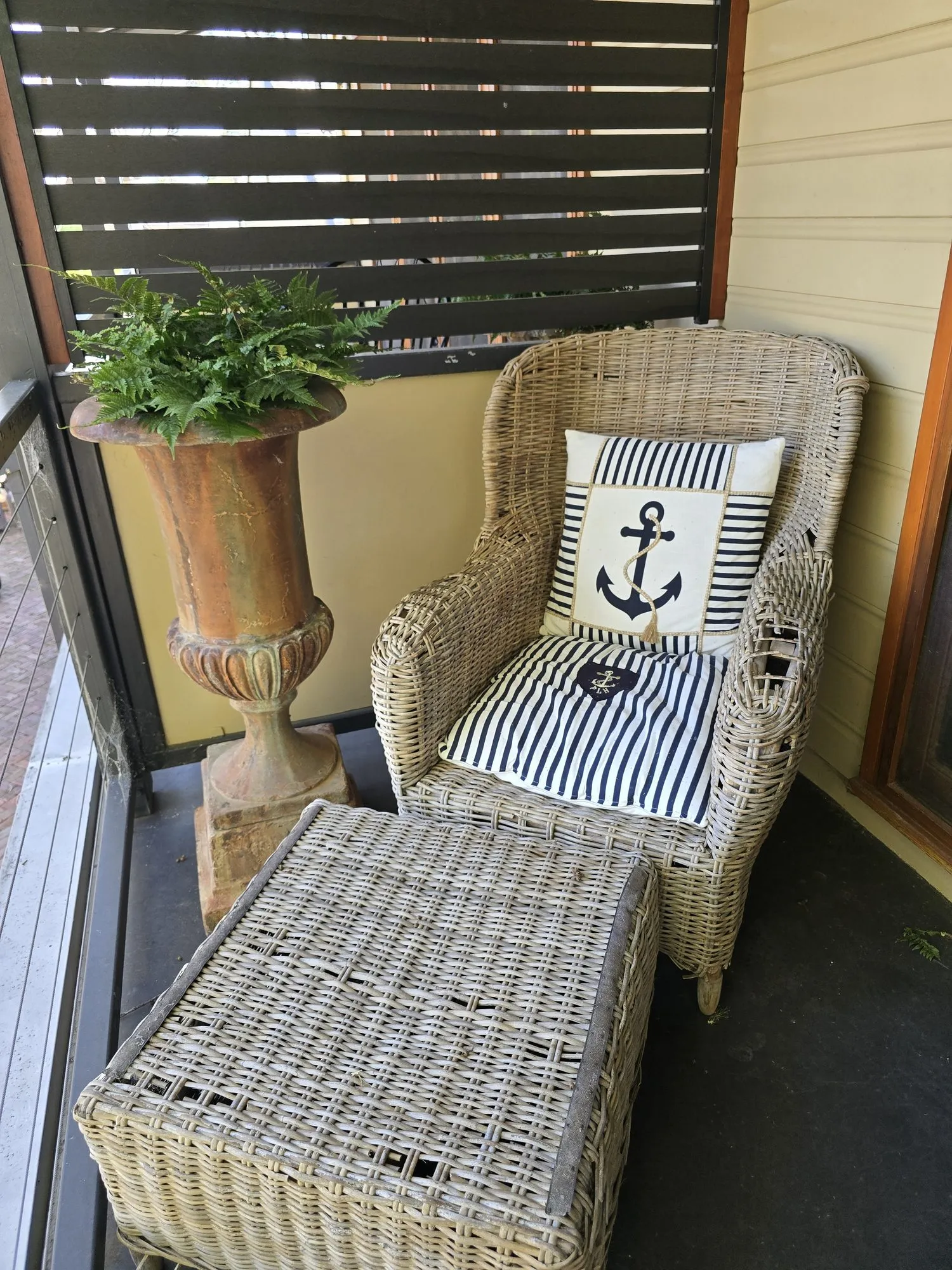 Wicker armchair and footstool with a nautical cushion on the balcony