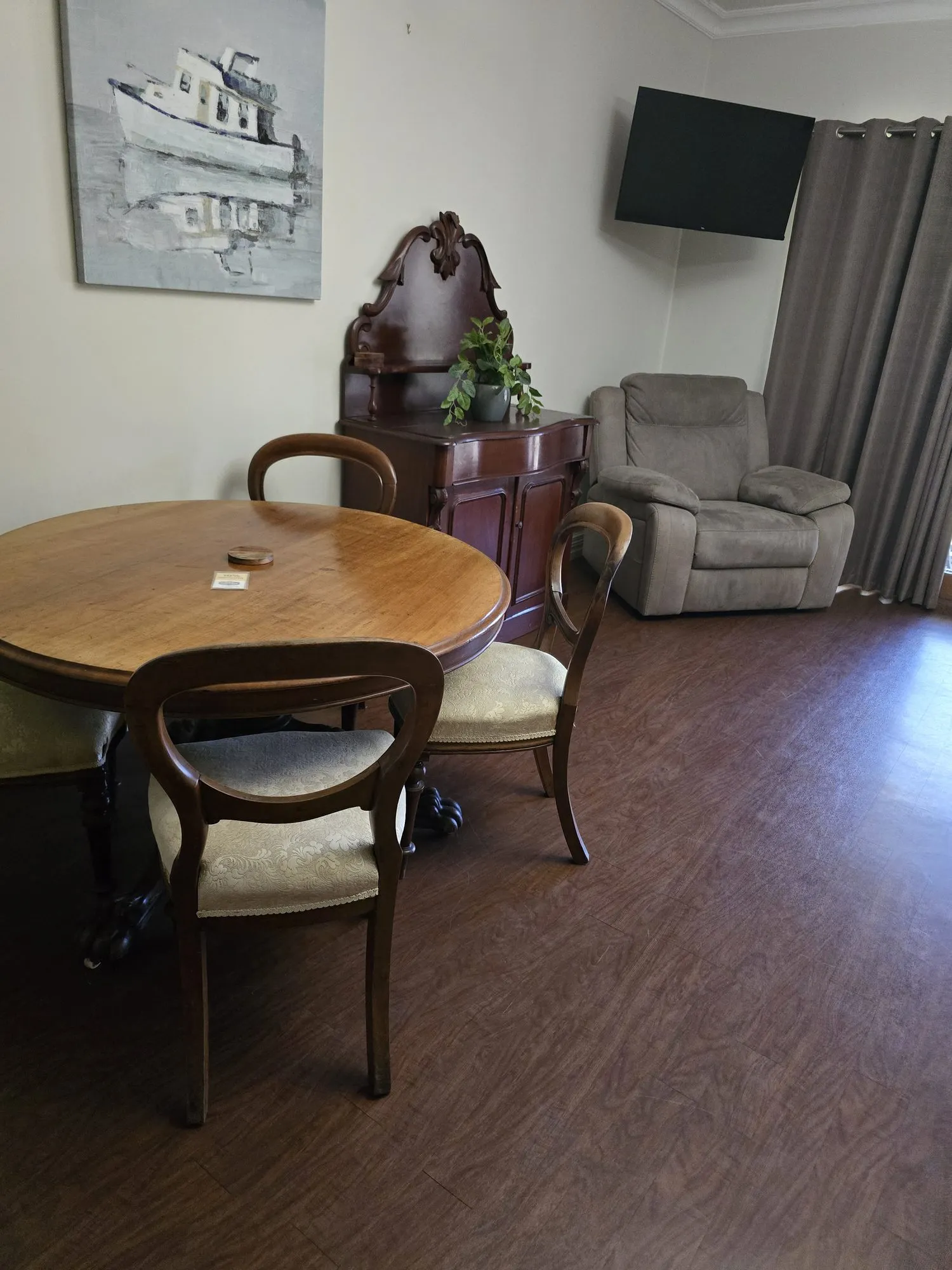 Round timber dining table with balloon-back chairs and an ornate dresser