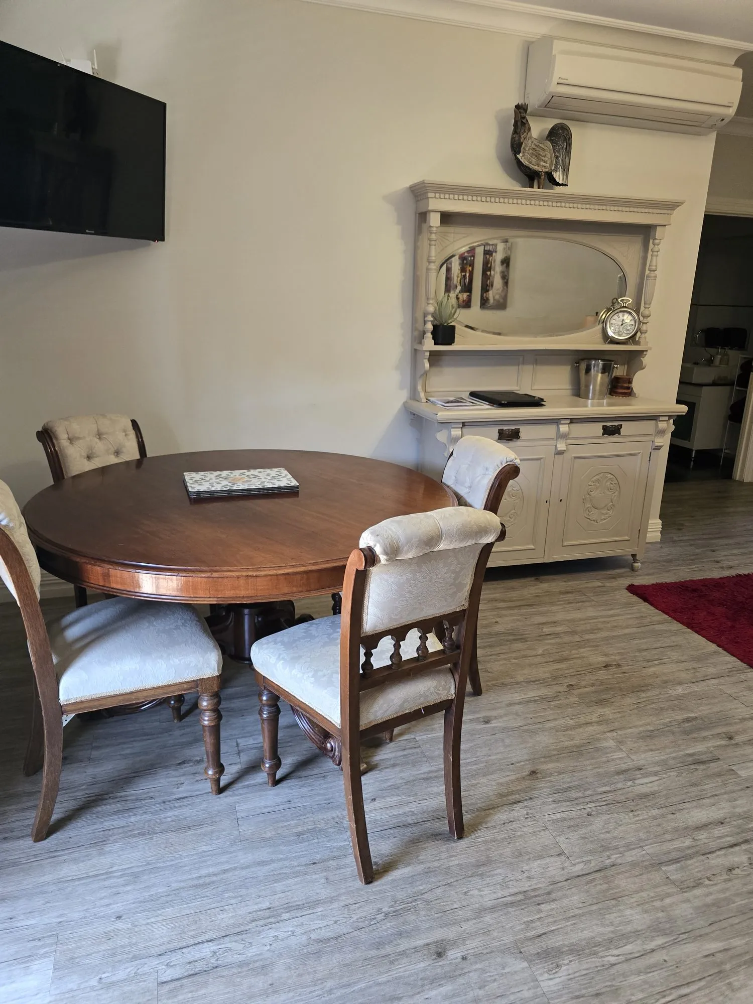 Round antique dining table with damask-upholstered chairs beside a painted mirror-backed dresser