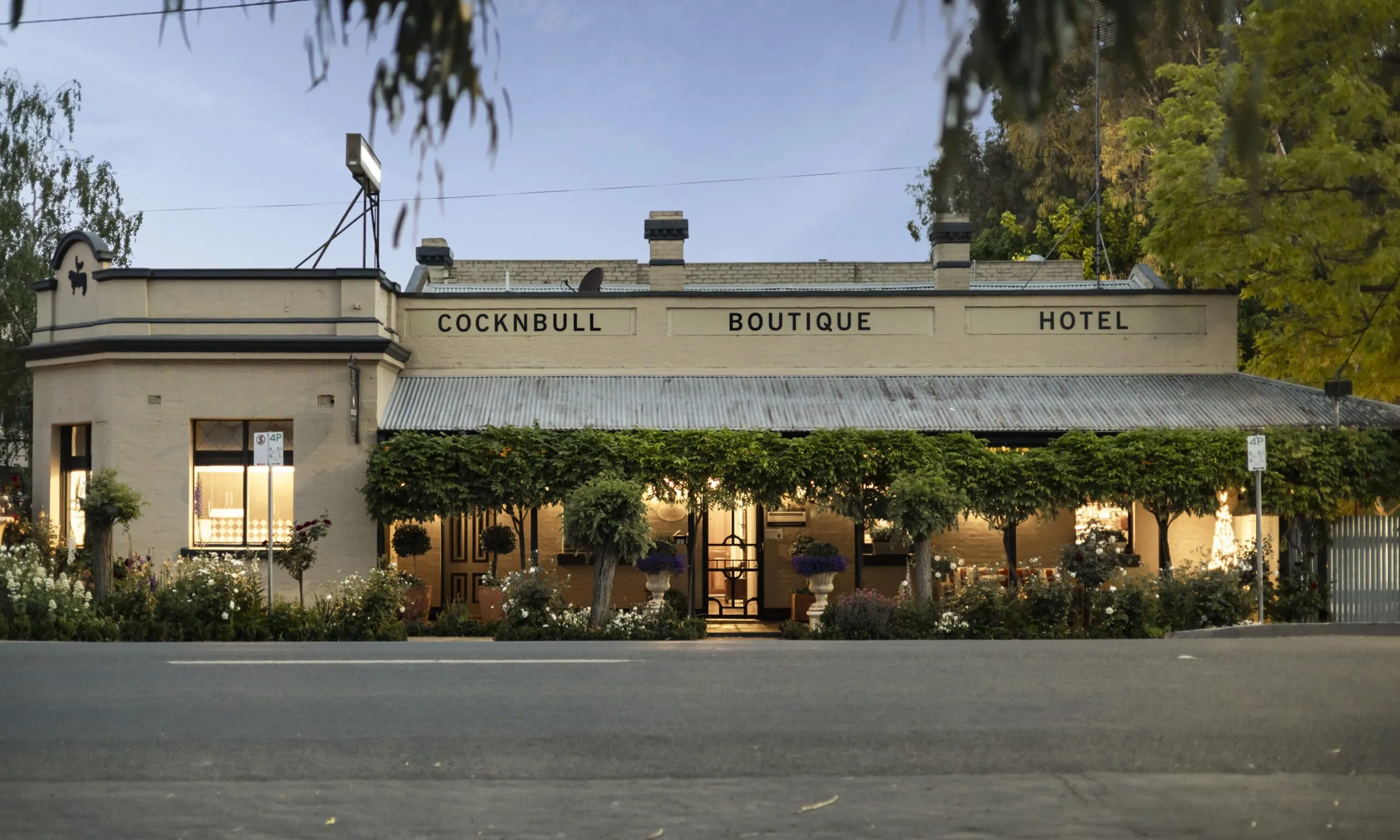 The CocknBull Boutique Hotel on Warren Street at dusk, its verandah lit behind a line of standard roses